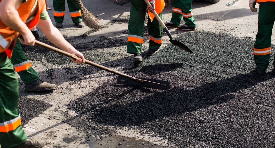 Workers on Asphalting paver machine during Road street repairing works. Street resurfacing. Fresh asphalt construction. Bad road