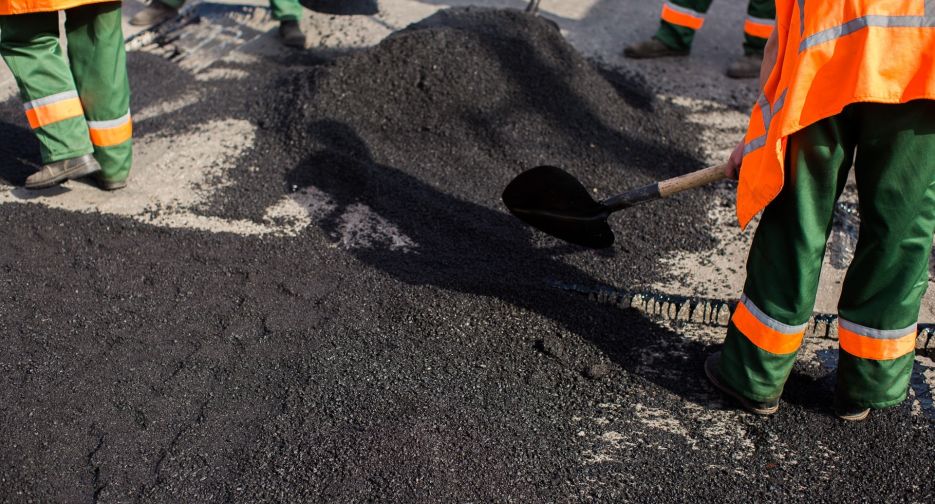 Workers on Asphalting paver machine during Road street repairing works. Street resurfacing. Fresh asphalt construction. Bad road